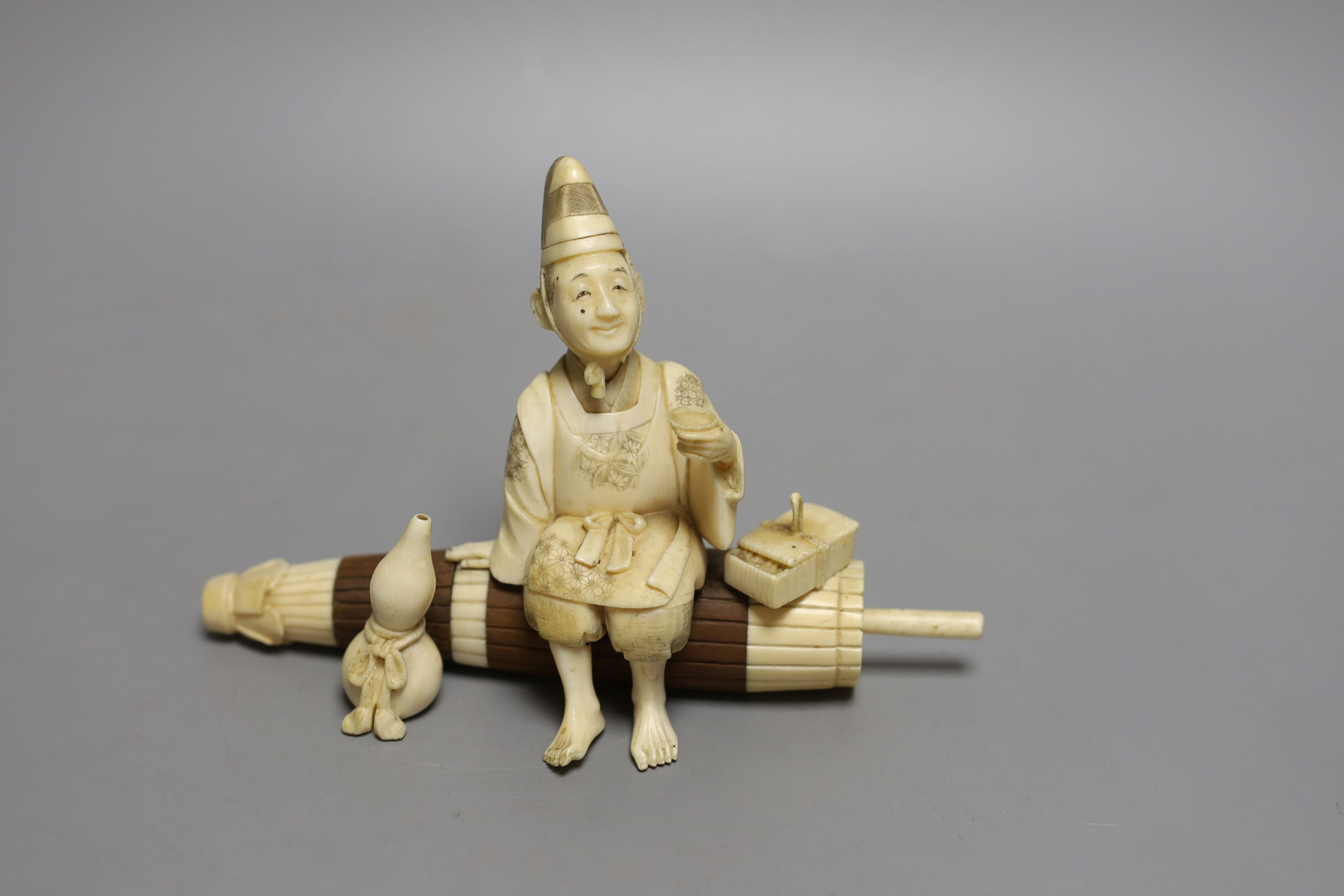 A Japanese ivory and wood okimono of a priest seated on a parasol, early 20th century, signed to a red lacquer tablet - 11cm tall